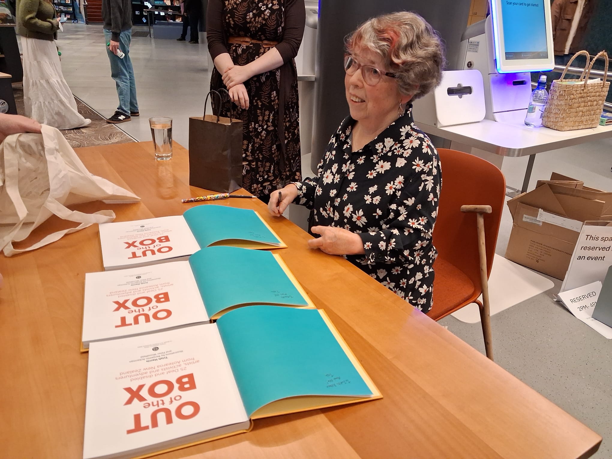 Trish Harris sits at a table, signing copies of her book at the book launch